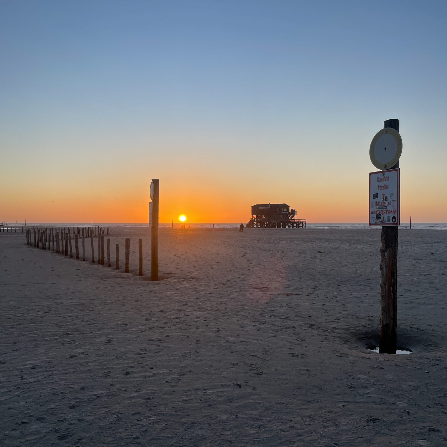 St. Peter-Ording auf Holz - Sonnenuntergang am Pfahlbau mit Schild